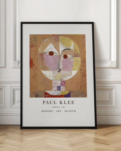 A framed museum poster of Paul Klee's 1922 painting 'Senecio'. The artwork is an abstract, geometric portrait of a human head in warm tones of orange, yellow, pink, and red against a textured brown background. The text 'PAUL KLEE', 'SENECIO - 1922', and 'MODERN - ART - MUSEUM' is printed below the image. Print