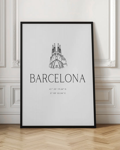 A minimalist black and white framed poster featuring a line art drawing of the Sagrada Familia. Below the drawing, the word 'BARCELONA' is printed in a large, thin sans-serif font, followed by the city's geographical coordinates. Artwork