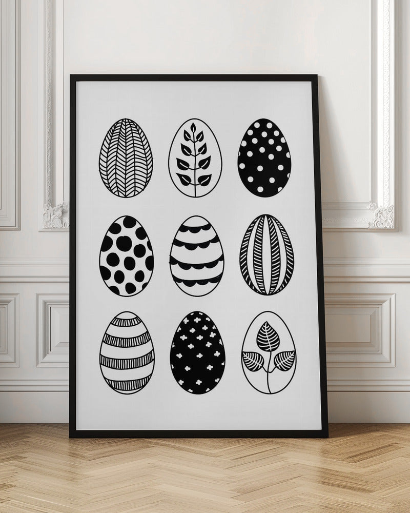 A black and white art print featuring a 3x3 grid of nine illustrated Easter eggs. Each egg has a unique, hand-drawn pattern, including polka dots, stripes, chevrons, florals, and leafy branches, all within a thin black frame. Poster
