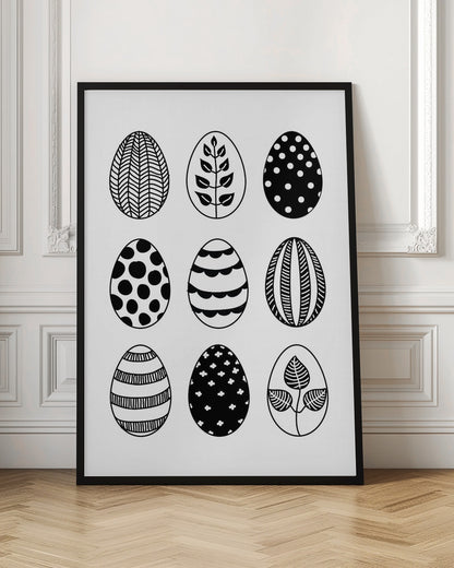 A black and white art print featuring a 3x3 grid of nine illustrated Easter eggs. Each egg has a unique, hand-drawn pattern, including polka dots, stripes, chevrons, florals, and leafy branches, all within a thin black frame. Poster