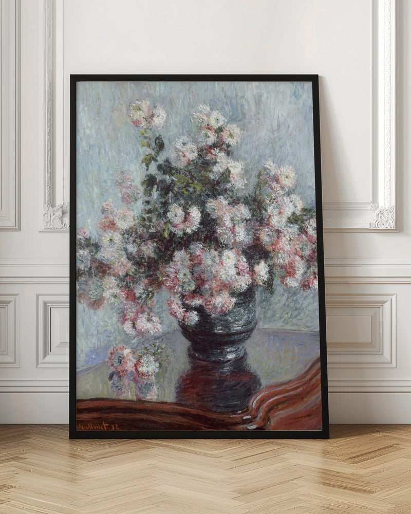 An impressionist painting by Claude Monet depicting a large bouquet of white and pink chrysanthemums in a dark, ornate vase. The vase sits on a reflective, reddish-brown wooden table, and the background is a textured light blue wall. The painting is framed in black. Artwork