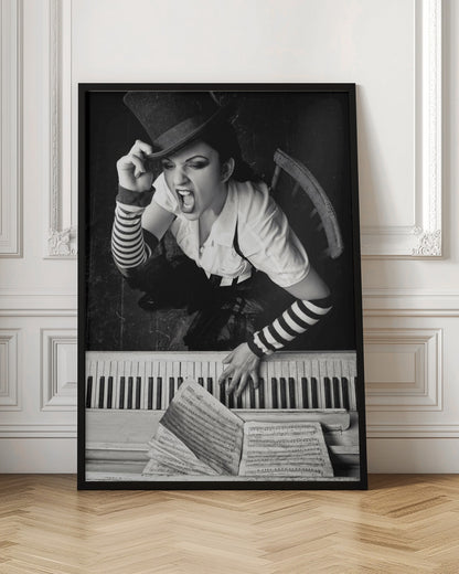 A dramatic black and white high-angle photograph of a woman in a top hat and striped arm warmers, shouting or singing passionately while seated at a piano with sheet music. Print