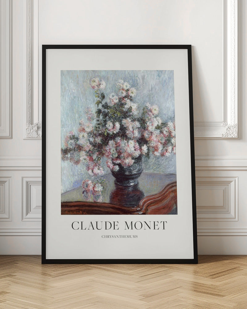 A framed art print of Claude Monet's impressionist painting, 'Chrysanthemums.' The painting features a lush bouquet of pink and white chrysanthemums in a dark vase resting on a reflective, mahogany-colored table against a light blue, textured background. The print includes a white border with the artist's name and the title below the artwork, all enclosed in a simple black frame. Print