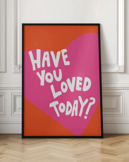 A framed art print with the text 'Have you loved today?' in a playful white font. The text is centered on a large pink heart which is set against a vibrant orange background. Artwork