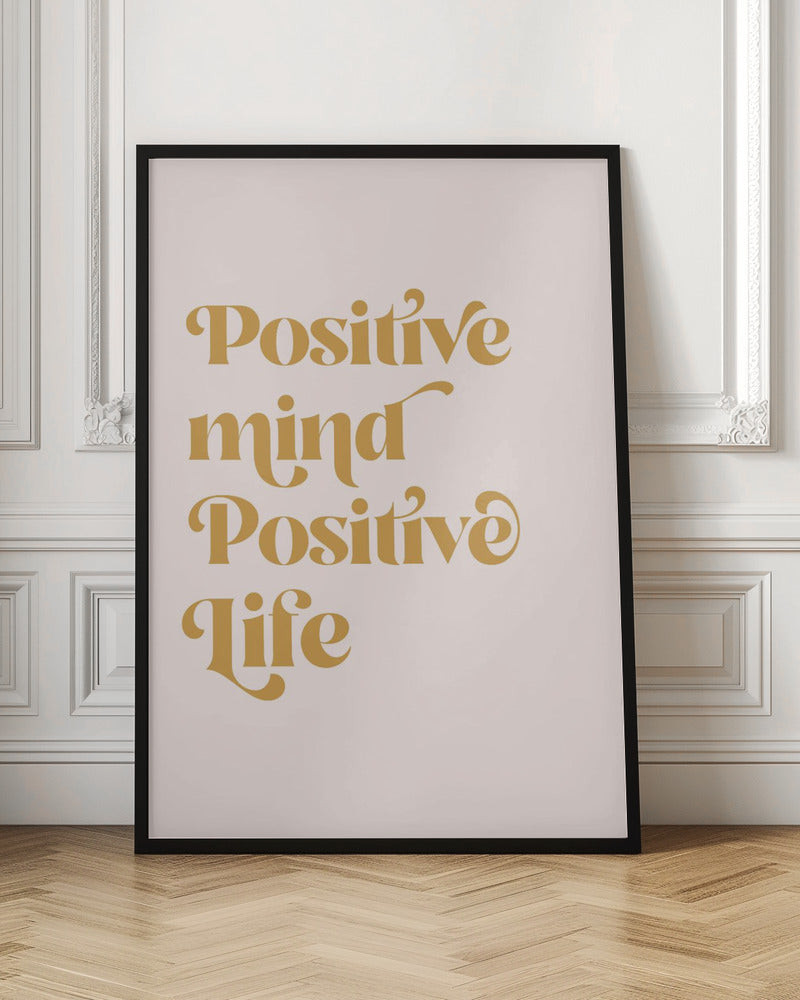 A framed art print featuring the motivational quote 'Positive mind Positive life' in a gold, retro-style font against a light pink background. The text is centered and arranged vertically. Artwork