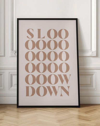 A minimalist art print with the phrase 'Slow Down' in a brown serif font against a pale pink background. The word is styled vertically, with 'SLOO' on the top line, followed by multiple lines of 'OOOO', and ending with 'OOW' and 'DOWN', visually stretching the word to emphasize the message. Artwork