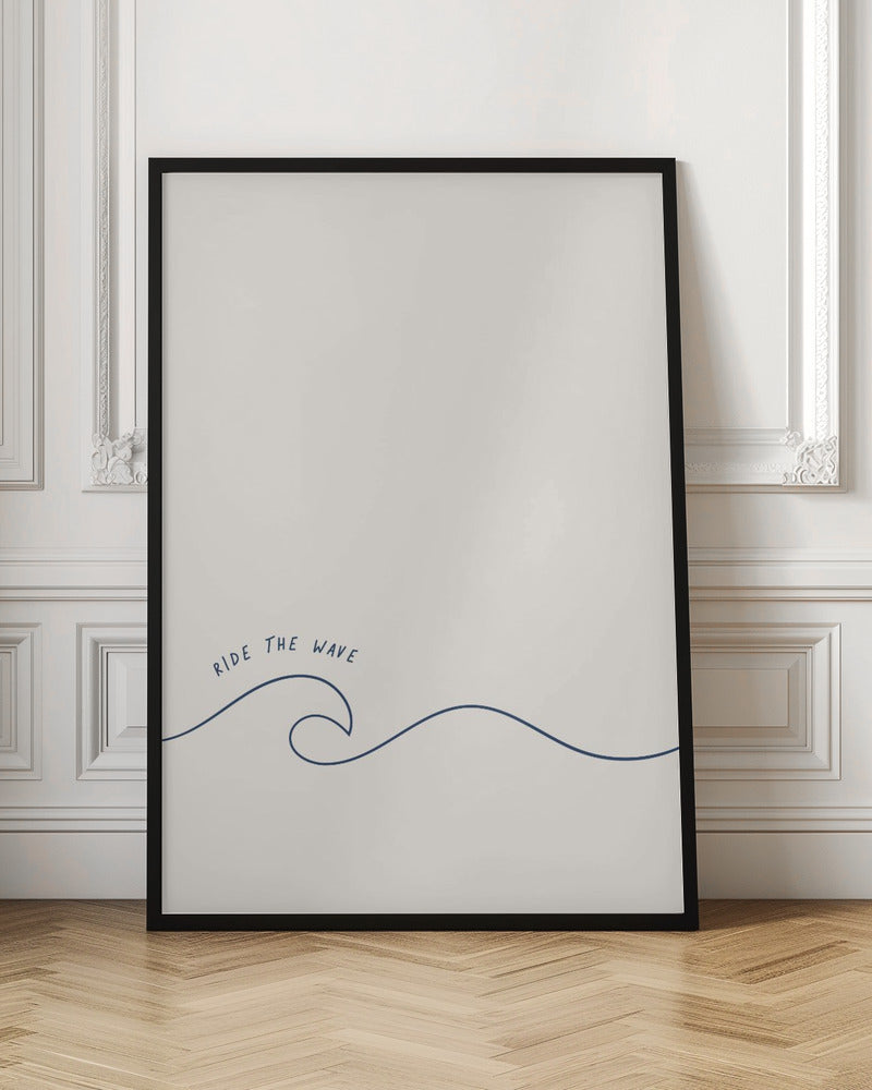 A minimalist art print in a black frame featuring a single dark blue line that forms a simple ocean wave on an off-white background. The words 'RIDE THE WAVE' are written in a casual, handwritten font above the crest. Wall Art