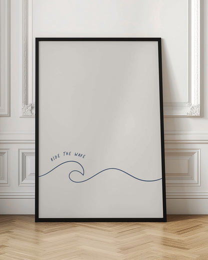 A minimalist art print in a black frame featuring a single dark blue line that forms a simple ocean wave on an off-white background. The words 'RIDE THE WAVE' are written in a casual, handwritten font above the crest. Wall Art