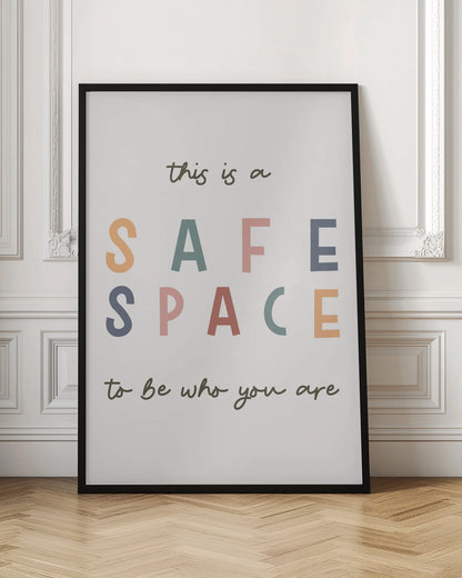 A framed poster with an inspirational message that reads 'this is a SAFE SPACE to be who you are'. The words 'SAFE SPACE' are in large, block letters of various muted colors like orange, sage, pink, and blue, while the rest of the text is in a smaller, dark green script font on an off-white background. Poster