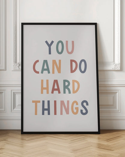 A framed poster featuring the inspirational quote 'YOU CAN DO HARD THINGS'. The text is in a simple, uppercase, sans-serif font with each letter in a different muted color, including shades of blue, green, pink, and orange, on a clean white background. Print
