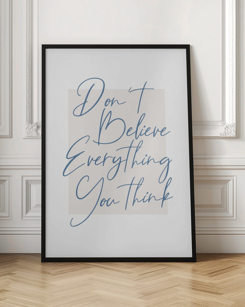 A minimalist art print in a black frame with the quote 'Don't Believe Everything You Think' written in blue cursive script. The text is set against a light beige rectangular background on a white canvas. Wall Art