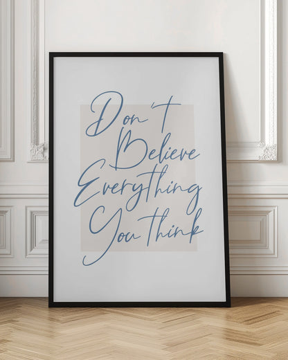 A minimalist art print in a black frame with the quote 'Don't Believe Everything You Think' written in blue cursive script. The text is set against a light beige rectangular background on a white canvas. Wall Art