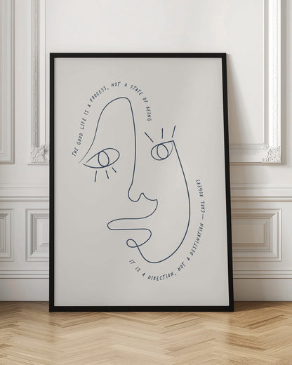 A minimalist art print in a black frame featuring a single dark blue continuous line drawing of an abstract face on a cream background. A quote by Carl Rogers is written along the curves of the face: "The good life is a process, not a state of being. It is a direction, not a destination." Poster