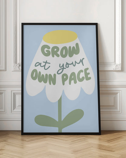 A motivational art print featuring a stylized white flower with a yellow center and green stem against a light blue background. The phrase 'GROW at your OWN PACE' is written in green, hand-drawn lettering across the flower's petals. Artwork