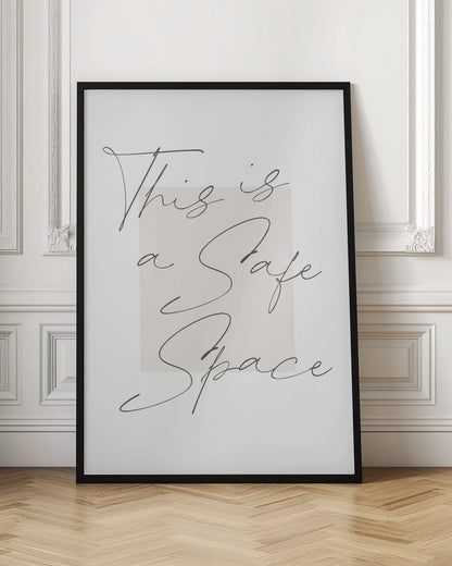 A minimalist art print in a black frame with the words 'This is a Safe Space' written in a flowing black cursive script over a pale beige rectangle on a white background. Artwork