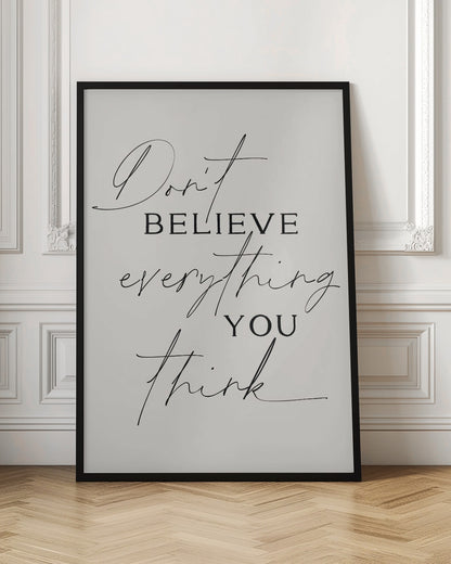 A minimalist art print with a thin black frame, featuring the quote 'Don't believe everything you think' in a mix of elegant script and serif fonts on a light beige background. Wall Art