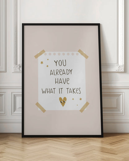 A motivational poster in a black frame with a pale pink background. A white piece of notebook paper is taped to the center with the handwritten text 'YOU ALREADY HAVE WHAT IT TAKES' in brown. It's decorated with small gold stars and a cute, smiling gold heart. Decor