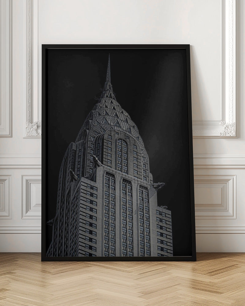 A dramatic, low-angle, black and white photograph of the top of the Chrysler Building, showcasing its iconic Art Deco spire and architectural details against a solid black background. Decor