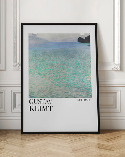 A poster of Gustav Klimt's painting 'Attersee', featuring a tranquil, impressionistic view of a lake with shimmering turquoise and green water under a muted blue and gray sky. The artwork is presented in a modern format with the artist's name and the painting's title below, all within a thin black frame. Poster