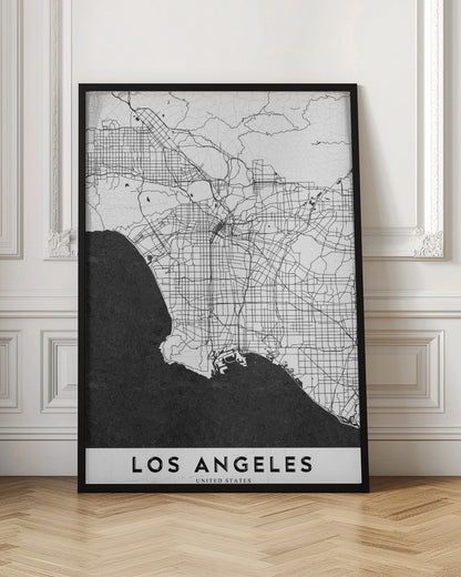 A minimalist black and white framed poster of a street map of Los Angeles. The land is white with an intricate grid of black lines representing roads and highways, while the Pacific Ocean is a solid, textured black. A white band at the bottom contains the city's name, 'LOS ANGELES', in a bold, black sans-serif font. Decor