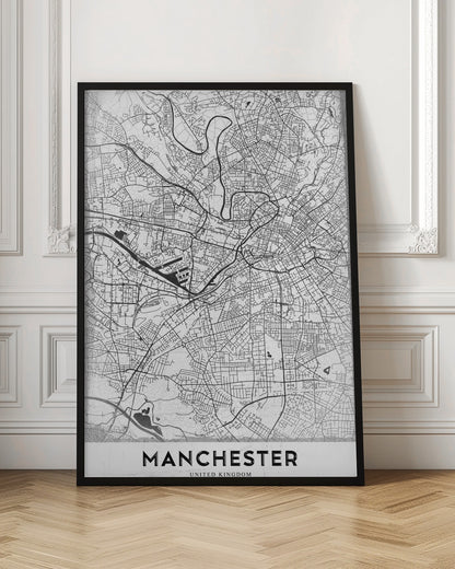 A minimalist black and white street map of Manchester, UK, displayed in a simple black frame. The map details the intricate network of roads and waterways, with the city's name 'MANCHESTER' printed in a bold, modern font at the bottom. Wall Art