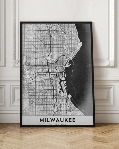 A minimalist, black and white street map of Milwaukee, displayed in a black frame. The map details the city's grid system, major roads, and waterways against a textured background, with the word 'MILWAUKEE' in a bold, sans-serif font at the bottom. Poster