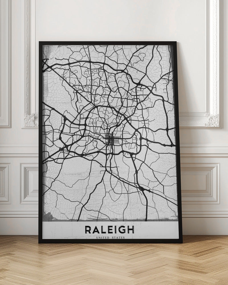 A minimalist black and white street map of Raleigh, North Carolina, displayed in a black frame. The map features black lines representing roads on a distressed, crackled white background. At the bottom, the word 'RALEIGH' is printed in a bold, black, sans-serif font. Print