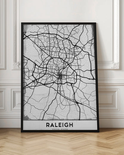 A minimalist black and white street map of Raleigh, North Carolina, displayed in a black frame. The map features black lines representing roads on a distressed, crackled white background. At the bottom, the word 'RALEIGH' is printed in a bold, black, sans-serif font. Print