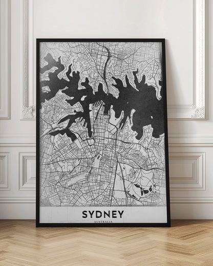 A modern black and white framed art print of a city map of Sydney, Australia. The water bodies are shown in solid textured black, while the land is depicted with a detailed white street grid. At the bottom, the word 'SYDNEY' is printed in bold capital letters. Poster