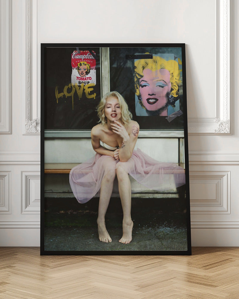 A blonde woman styled like Marilyn Monroe sits on a bench, wearing a pink tulle skirt. Behind her, a dark window features an Andy Warhol-style poster of Monroe, a Campbell's soup can parody, and the word 'LOVE' in gold graffiti. Artwork
