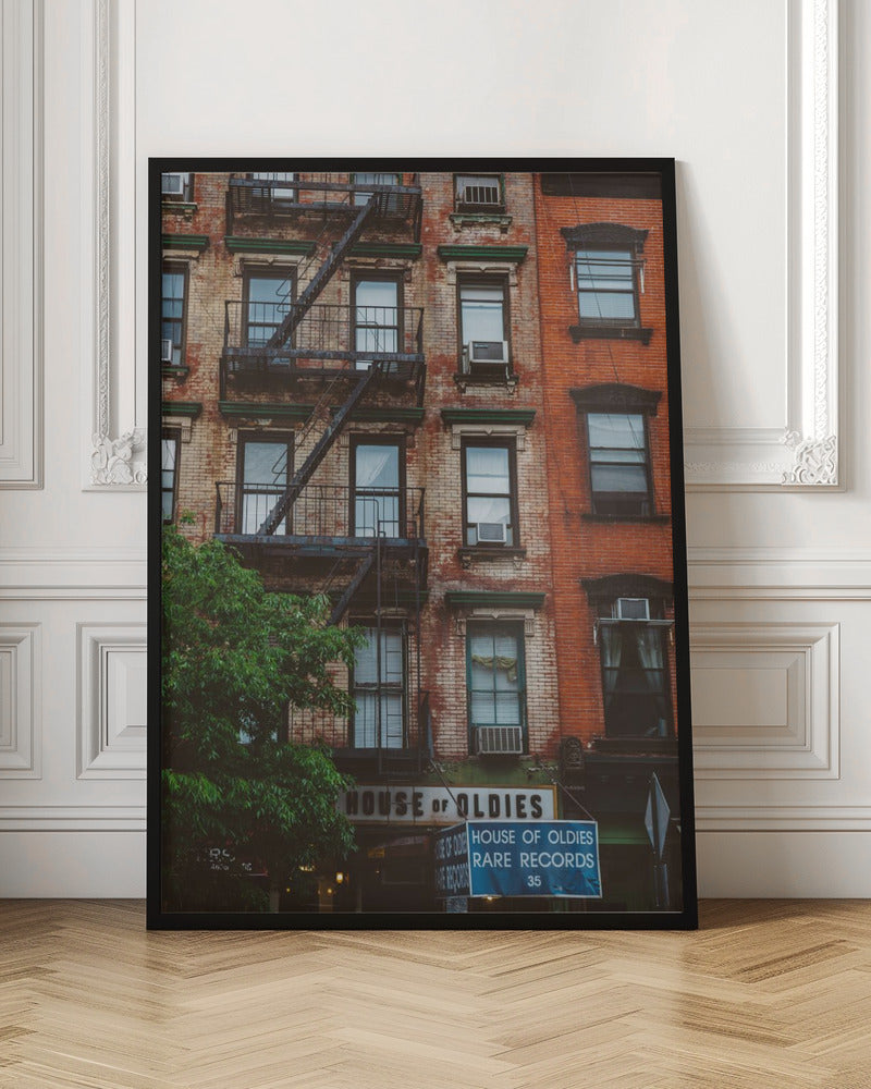 A classic multi-story brick apartment building with a prominent black metal fire escape zigzagging across its facade. A sign for a 'House of Oldies' rare records shop is visible on the ground floor. Poster