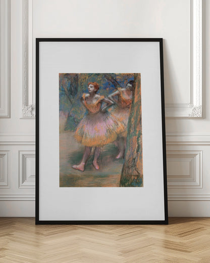 A framed vertical print of Edgar Degas's impressionist pastel drawing 'Dancers, Pink and Green'. It depicts two ballerinas in pink and orange tutus standing backstage amongst trees, captured in soft, expressive strokes. Artwork