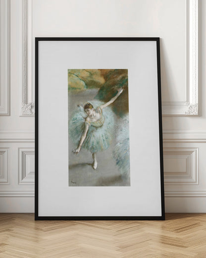 A framed vertical reproduction of an Edgar Degas painting showing a ballerina from a high angle. She wears a voluminous light blue tutu and is posed gracefully with arms outstretched against a soft, impressionistic background of earthy browns and tans. Poster