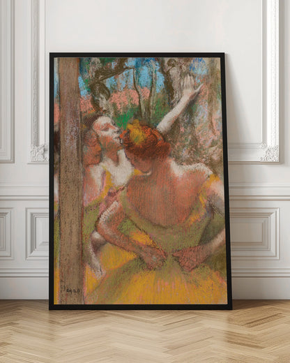 An Impressionist pastel drawing by Edgar Degas depicting several ballet dancers backstage. A dancer with reddish-orange hair is seen from behind in a yellow-green costume, while another dancer stretches an arm upwards. The background is a textured blend of blue, pink, and green. Decor
