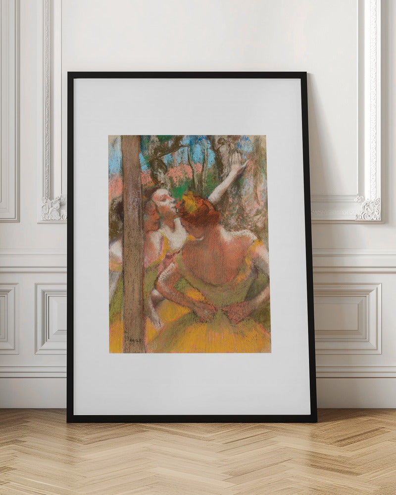 A framed art print of an impressionistic pastel painting by Edgar Degas featuring several ballet dancers backstage. A central figure, seen from behind, adjusts her yellow-green tutu while other dancers stretch in the background. Artwork