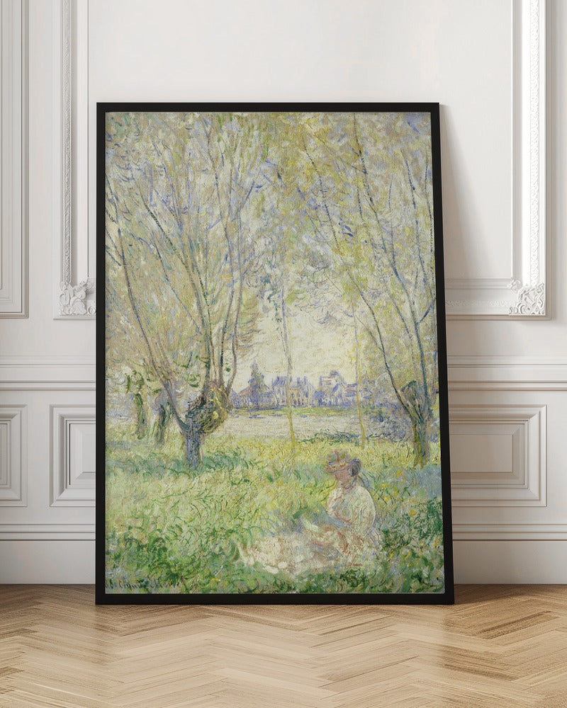 An Impressionist painting, 'Springtime' by Claude Monet, showing a woman in a hat sitting in a sunlit green field. Slender trees with light green foliage frame a view of a village across a river, evoking a peaceful spring day. The artwork is presented in a simple black frame. Artwork