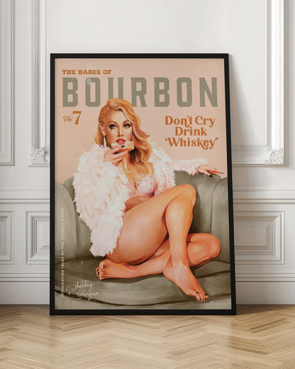 A vintage-style pin-up poster titled 'The Babes of Bourbon, Vol 7'. A glamorous blonde woman in a pink bra and fluffy white coat lounges on a gray-green sofa, holding a glass of whiskey. The poster also has the text 'Don't Cry Drink Whiskey'. Wall Art