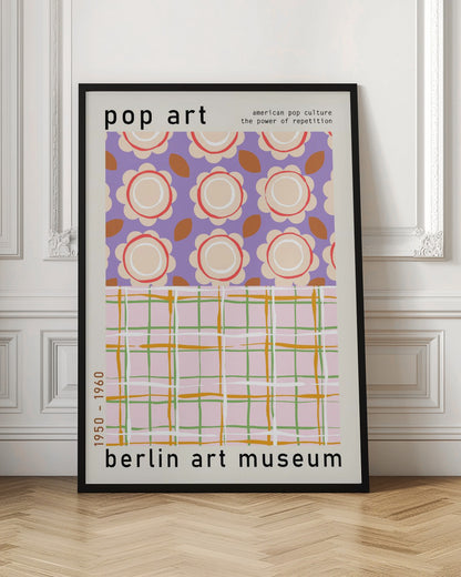 A framed pop art museum poster advertising an exhibition at the Berlin Art Museum. The poster features two distinct patterns. The top section has repeating stylized cream and red flowers on a purple background, with the words 'pop art' and 'american pop culture the power of repetition'. The bottom section displays a pink, green, and orange plaid pattern. The dates '1950 - 1960' are printed vertically on the side. Artwork