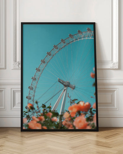 A low-angle shot of the London Eye ferris wheel against a clear, vibrant teal sky. In the foreground, out-of-focus orange flowers create a soft, colorful frame. Poster