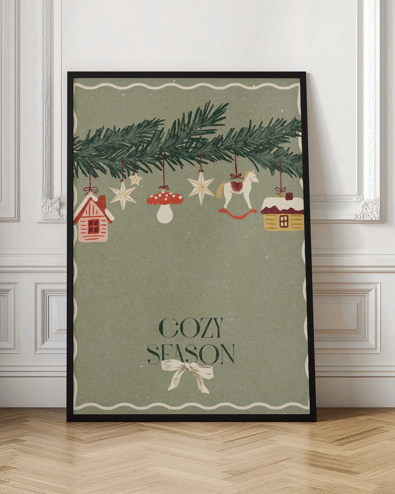 A vintage-style holiday poster with a sage green background. A pine branch hangs at the top, decorated with illustrated ornaments including houses, stars, a mushroom, and a rocking horse. Below, the text 'COZY SEASON' is written in a dark serif font with a light-colored bow underneath. Artwork