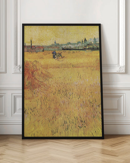 A Post-Impressionist painting by Vincent van Gogh depicting a vast, golden wheat field under a yellow sky. Two figures are harvesting wheat in the middle distance, with a town and industrial buildings on the horizon. The artwork is characterized by thick, textured brushstrokes and is displayed in a black frame. Print
