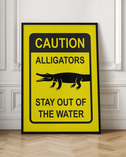 A yellow and black rectangular warning sign in a black frame. The sign reads 'CAUTION ALLIGATORS' at the top, features a black silhouette of an alligator in the center, and says 'STAY OUT OF THE WATER' at the bottom. Decor