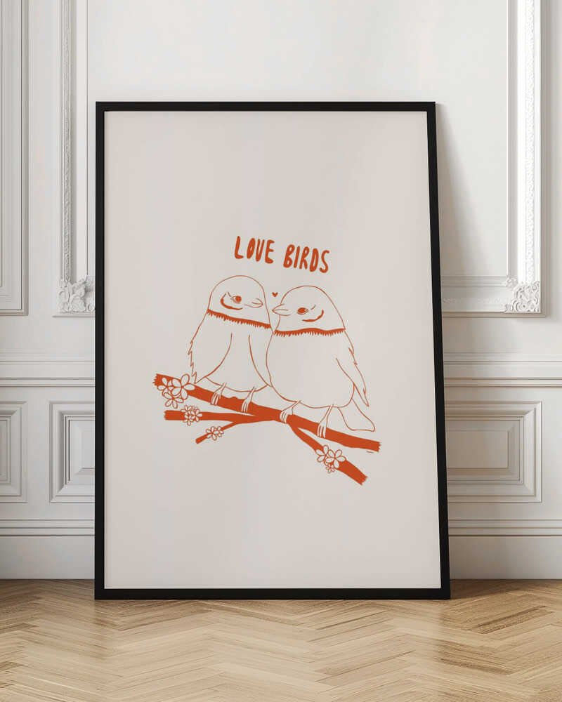 A framed art print featuring a minimalist, reddish-orange illustration on a cream background. Two cartoonish, plump birds sit close together on a flowering branch, looking at each other affectionately. Above them, the text 'LOVE BIRDS' is written in a playful, rounded font. Decor