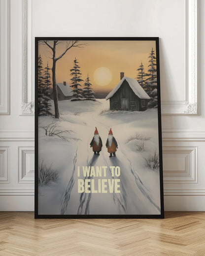 A vertical painting of a snowy winter scene with two gnomes walking away from the viewer on a path. The gnomes have long white beards and red hats. In the distance are snow-covered cabins and pine trees under an orange sunset sky. The words 'I WANT TO BELIEVE' are written in large, bold letters in the foreground. Print