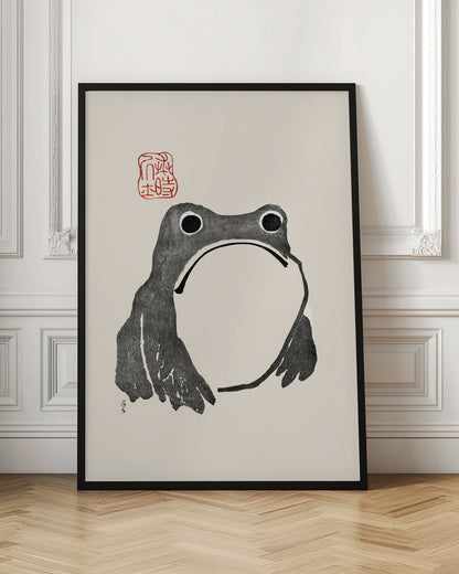 A minimalist Japanese-style ink wash painting of a stylized frog with a grumpy expression. The frog is rendered in black ink on a cream-colored paper, with a large white throat pouch. A red artist's seal is stamped above the frog's head. The artwork is presented in a simple black frame. Artwork