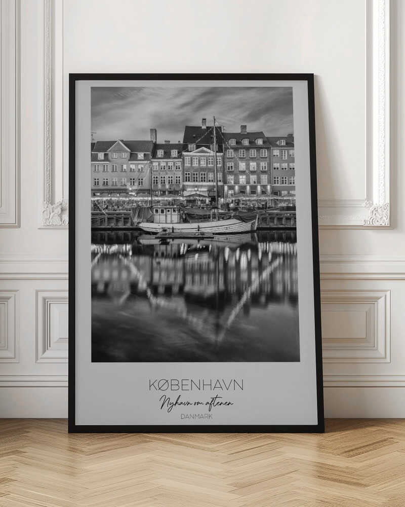 A black and white poster of Nyhavn harbor in Copenhagen at night. Historic buildings with glowing windows line the canal, and their lights create shimmering reflections in the water. A boat is docked in the foreground. The poster has text at the bottom that reads 'KØBENHAVN, Nyhavn om aftenen, DANMARK'. Poster