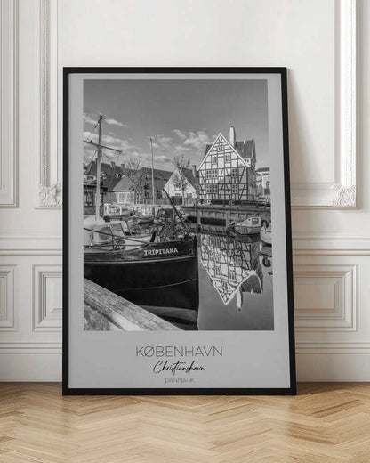 A black and white travel poster featuring a photo of Christianshavn in Copenhagen. The scene shows a boat named 'TRIPITAKA' docked in a canal, with a prominent half-timbered building across the water, its reflection visible on the surface. The bottom of the poster has text that reads 'KØBENHAVN', 'Christianshavn', and 'DANMARK'. Artwork