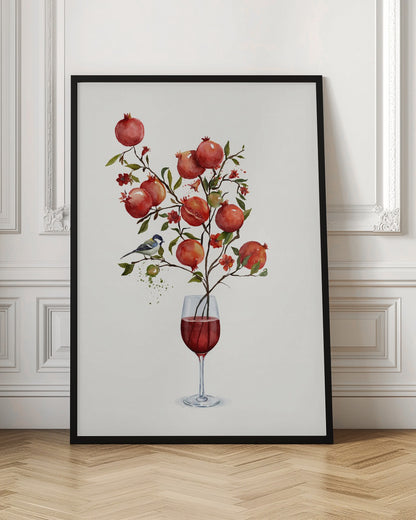 A surreal watercolor painting of a pomegranate branch growing out of a glass of red wine. The branch is laden with ripe red pomegranates, small red blossoms, and green leaves. A small blue and white bird is perched on a twig. The background is a clean, solid white, and the entire image is framed in black. Wall Art