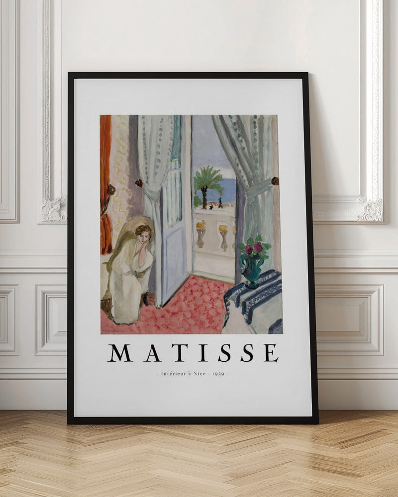 A framed art print of Henri Matisse's painting 'Intérieur à Nice - 1939'. The painting depicts a woman in a white robe sitting in a sunlit room with an open door leading to a balcony overlooking the sea and a palm tree. The poster has a white border with the artist's name and the title below the artwork. Artwork