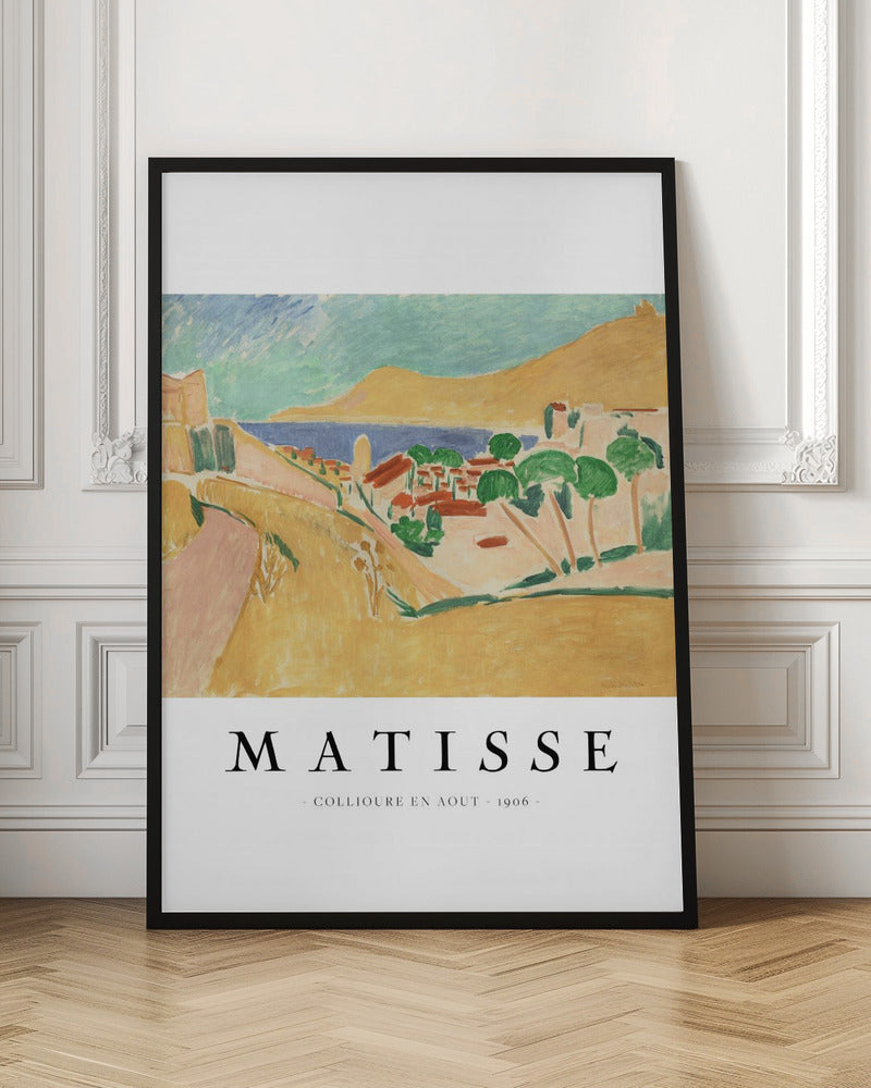 A poster featuring Henri Matisse's 1906 painting, 'Collioure en Aout'. The Fauvist artwork depicts a vibrant coastal landscape with yellow hills, a seaside village with red roofs, green trees, and a blue and turquoise sea. The poster has a black frame and white border with the artist's name and title underneath. Artwork